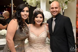 Quinceañera con corona, su madre y su padre posando sonrientes en una fiesta elegante de XV años.
