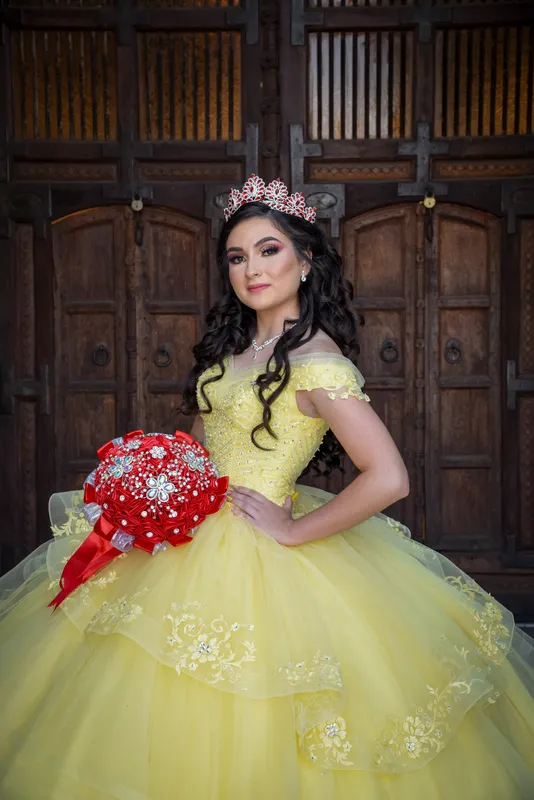 Quinceañera con vestido amarillo y ramo rojo posando frente a puerta de madera rústica en Phoenix.