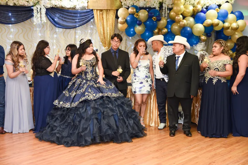 Quinceañera con vestido azul marino y familia celebrando con brindis frente a decoración de globos en Phoenix.