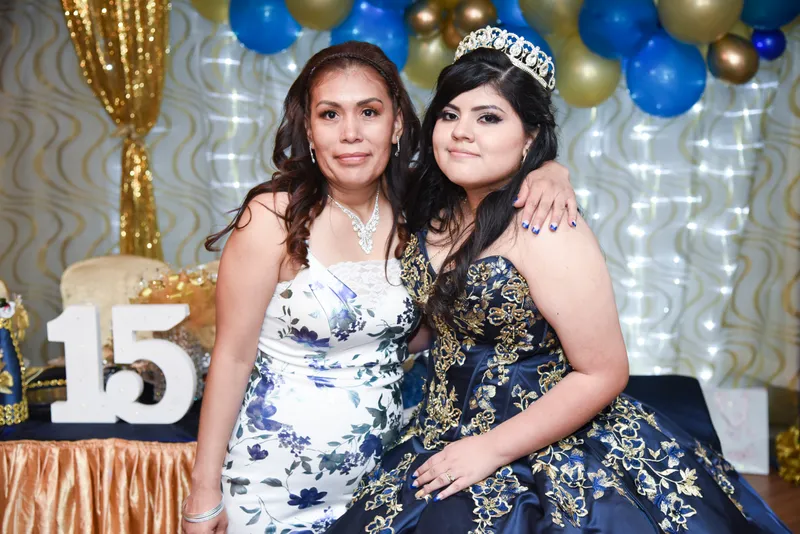 Quinceañera con vestido azul y corona posando con su madre frente a una decoración de globos en Phoenix.