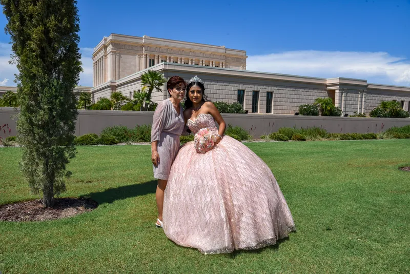 Quinceañera con vestido rosa brillante posando con una adulta frente al Templo de Mesa en un día soleado.