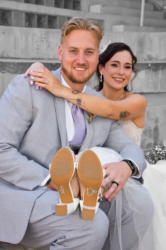Recién casados sonriendo mientras ella muestra las suelas de sus zapatos con la frase I Do escrita